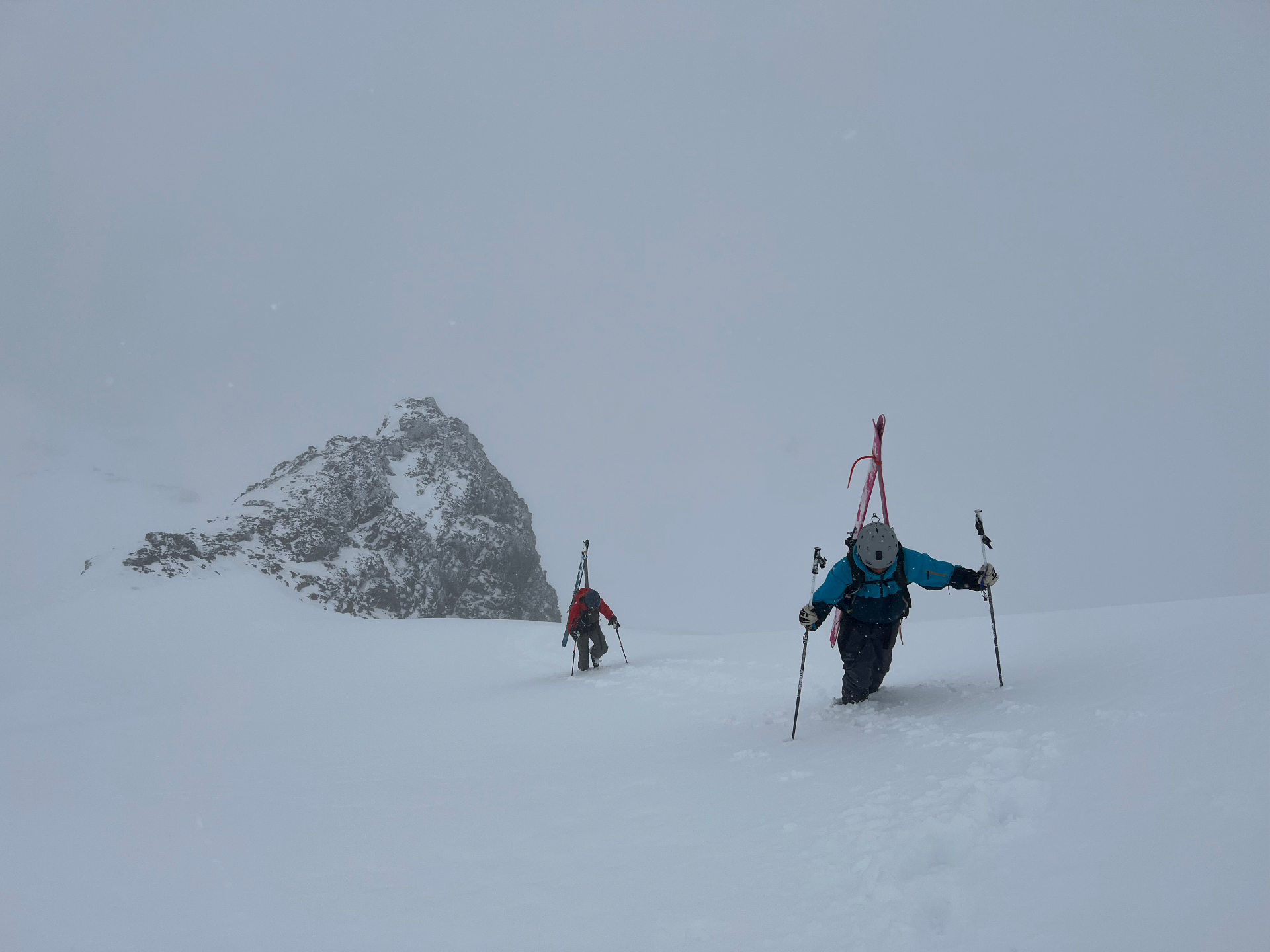 Two skiers carrying their gear across a snowy mountain ridge in stormy conditions