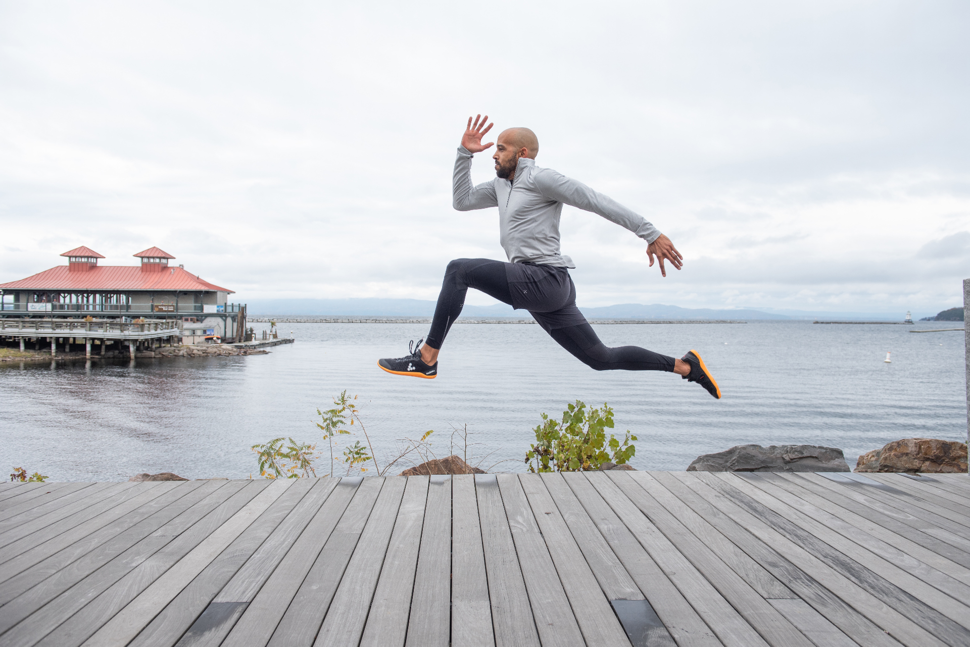 Frank mid-stride leaping along a lakeside boardwalk — embodying the practice of movement.
